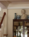 photo of plaster cast sculpture of male head of Cicero with squared bust and white and blue vases on a dark wood bookcase against a tan wall and staircase to the left