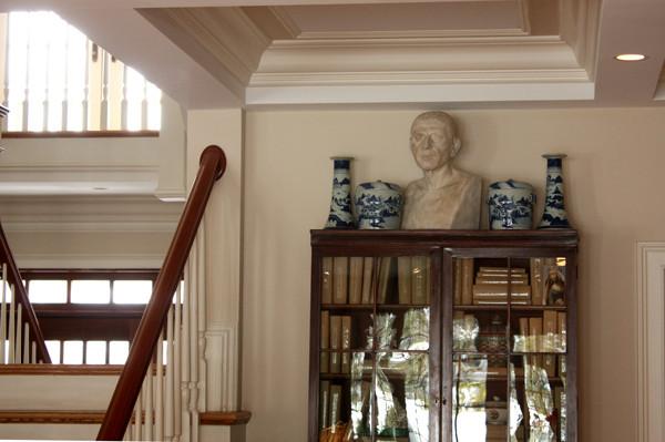 photo of plaster cast sculpture of male head of Cicero with squared bust and white and blue vases on a dark wood bookcase against a tan wall and staircase to the left