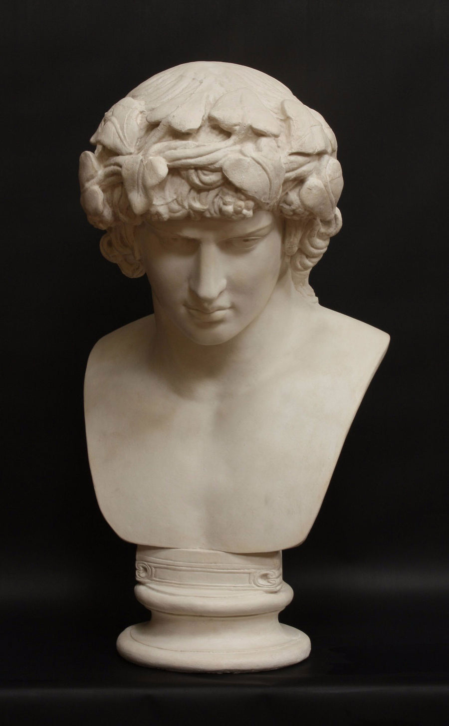 photo with black background of plaster cast of male bust of Antinous with crown of leaves
