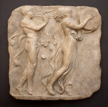 Photo of stone-colored plaster cast relief sculpture of two figures dancing in a procession against a black background