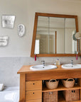 Photo of a bathroom with double sink and mirror with a white wall and four plaster cast sculptures of the left eye, left ear, nose, and mouth from Michelangelo's David statue hanging on the wall
