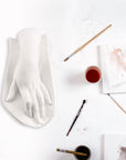 Photo of a plaster cast of a female hand on a white table with paintbrushes, paints, and paper