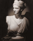 Photo of Cast Drawing of Plaster Caproni Cast of female bust on a table with a cloth over it and rolled into folds beside the statue with a black background