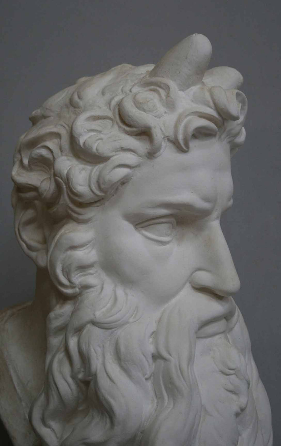 closeup photo of plaster cast bust of man, namely Moses, with curly hair and so-called horns and long beard on gray background