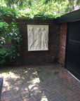 photo of plaster cast of ancient relief with three figures, namely Hades, Eurydice, and Orpheus, on a brick wall outdoors with trees behind, brick paving, and black door to the right