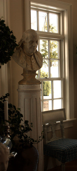 Photo of male bust sculpture on tall pedestal next to a window in a dining room