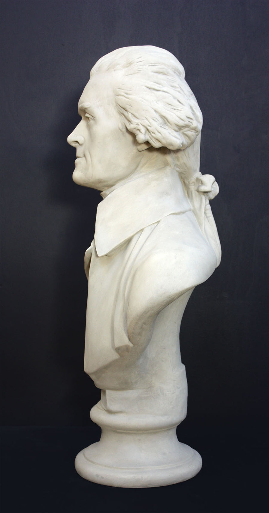 Photo of plaster cast bust sculpture of man with coat and neckerchief, namely Thomas Jefferson, with dark gray background