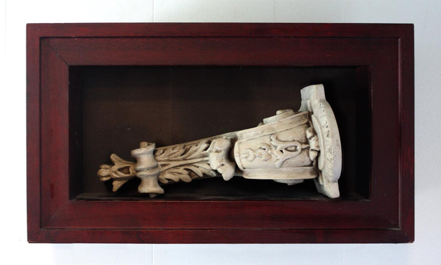 Photo of plaster sculptural ornament laying on it's side in a wooden shadowbox hanging on the wall