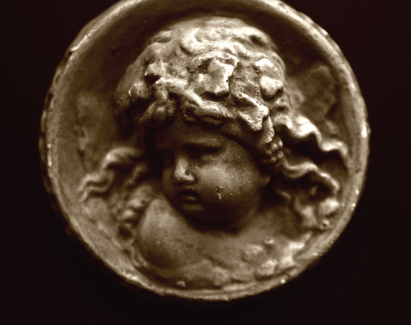 Photo of small round plaster sculpture medallion of head of an infant on a black background