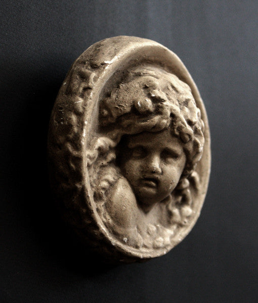 Photo of a side view of a small round plaster sculpture medallion of head of an infant on a black background