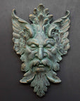photo of verdigris-colored plaster cast sculpture relief of moustached man's face made of leaves with gray background