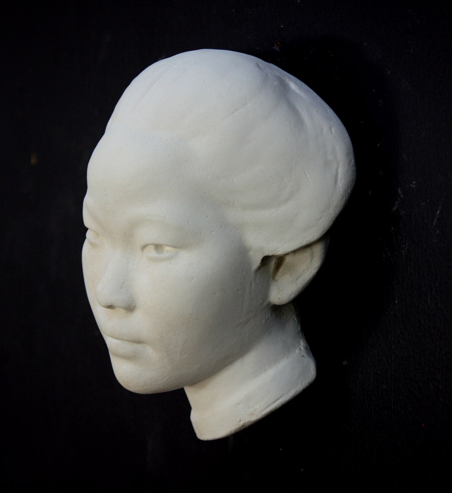Photo of plaster cast of face of Chinese female, profile view, on a black background
