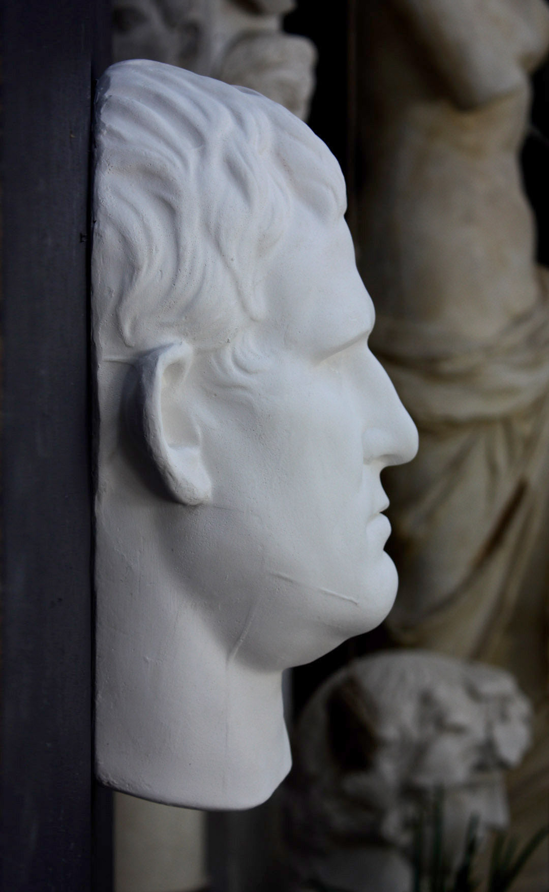 Photo of plaster cast sculpture reproduction of an Ancient Roman mask of Agrippa, side view, on a black background