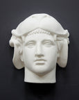 photo of white plaster cast of ancient sculpture of head, namely Omphale or Hercules, wearing Nemean lion skin against dark gray background