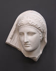photo of white plaster cast of ancient relief sculpture of female head with headpiece and covering against dark gray background