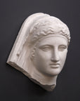 photo of white plaster cast of ancient relief sculpture of female head with headpiece and covering against dark gray background