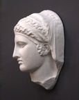 photo of white plaster cast of ancient relief sculpture of female head with headpiece and covering against dark gray background