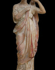 photo of plaster cast statue of female in pink robes with left arm raised and holding robe against black background