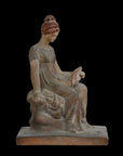 Photo of plaster cast sculpture of female in green-brown tinted robes seated with opened book against black background