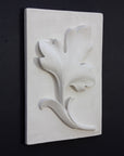 Photo of a plaster cast of a rectangle slab with a study of an acanthus leaf poited upward on the front, the whole object turned to the face the right to be seen at a 3/4 view, on a black background