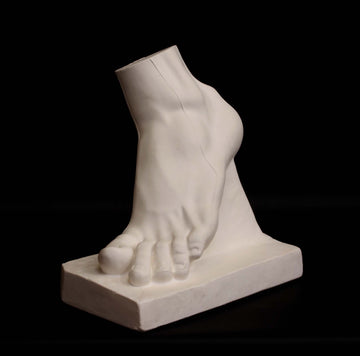 Photo of plaster cast sculpture of foot on a black background