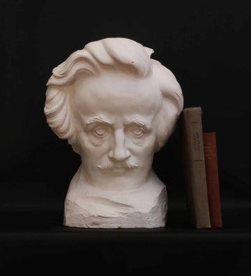 photo of plaster cast sculpture of man's head, namely Edgar Allan Poe, on a base with two books leaning against it on a black background
