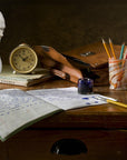 photo of dark wooden desk with open notebook and pen and ink, jar of pencils, small clock, leather bag, books, and plaster cast bust of Alexander Hamilton