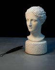 photo of plaster cast of ancient female bust, namely the goddess Diana, with a gray and black background and sculpting tool beside it