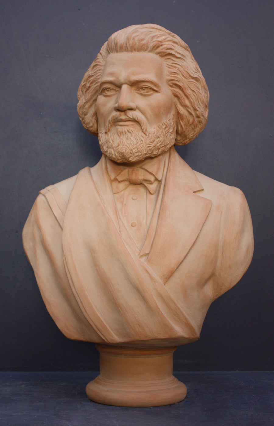 photo of terracotta-colored plaster cast sculpture of bust of Frederick Douglass with beard and in suit coat with toga over one shoulder on dark gray background