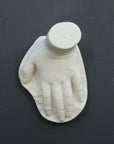 photo of white plaster cast sculpture of child hand against gray background