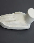 photo of white plaster cast sculpture of child hand against gray background