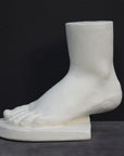 photo of white plaster cast sculpture of child foot against gray background