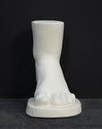 photo of white plaster cast sculpture of child foot against gray background