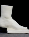 photo of white plaster cast sculpture of child foot against gray background