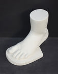 photo of white plaster cast sculpture of child foot against gray background