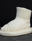 photo of white plaster cast sculpture of baby foot against gray background