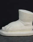 photo of white plaster cast sculpture of baby foot against gray background