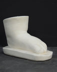 photo of white plaster cast sculpture of baby foot against gray background