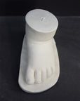 photo of white plaster cast sculpture of baby foot against gray background