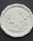 photo of white plaster cast relief sculpture of a child dancing and a female figure playing an instrument against dark gray background