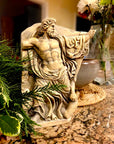 photo of plaster cast relief fragment of man, namely the god Zeus, on a red-orange granite counter leaning against a stone bowl with a plant visible on its left and a vase of flowers on its right