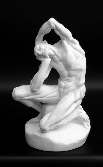 Photo of plaster cast sculpture of flayed man kneeling with hands on head on black background