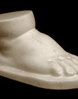 photo of off-white plaster cast sculpture of baby foot against black background