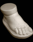 photo of off-white plaster cast sculpture of baby foot against black background
