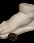 photo of off-white plaster cast sculpture of baby foot against black background
