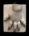 photo of off-white plaster cast sculpture of baby hand on panel against black background