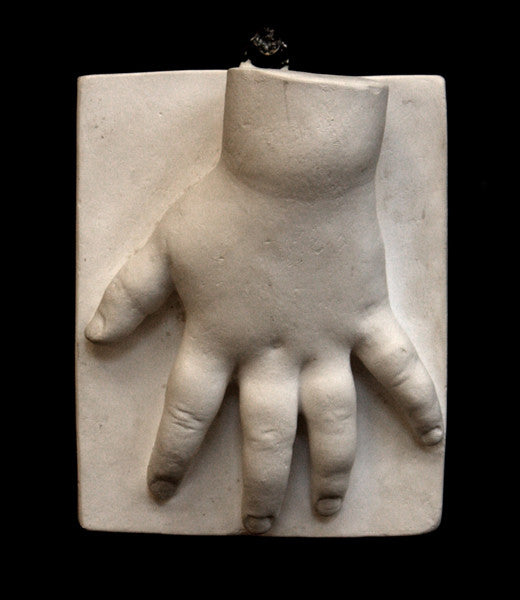 photo of off-white plaster cast sculpture of baby hand on panel against black background