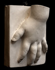 photo of off-white plaster cast sculpture of baby hand on panel against black background