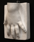 photo of off-white plaster cast sculpture of baby hand on panel against black background