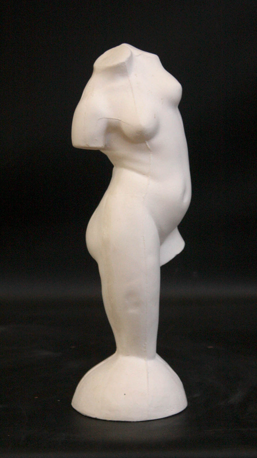 photo of plaster cast sculpture of female torso and right leg flowing into plaster base against black background